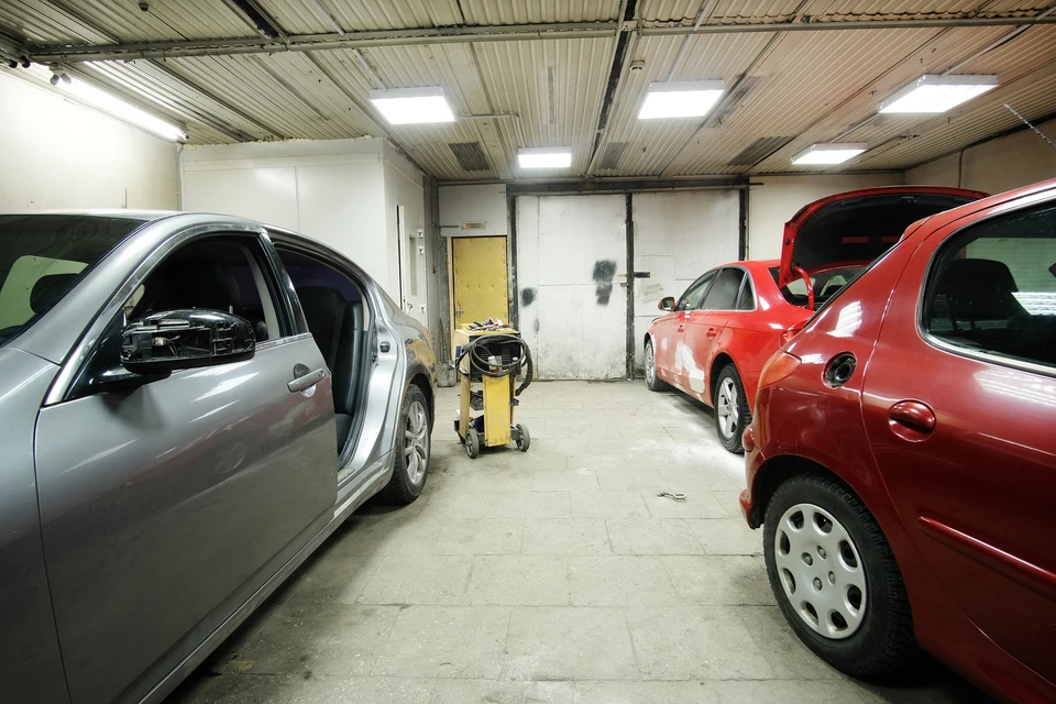 Intérieur d'un garage automobile avec deux véhicules en réparation, une berline grise et une rouge avec capot ouvert