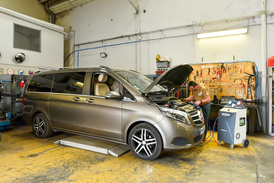 Deux techniciens en combinaison de travail bleue installent un pare-brise automobile dans un atelier de réparation vitré