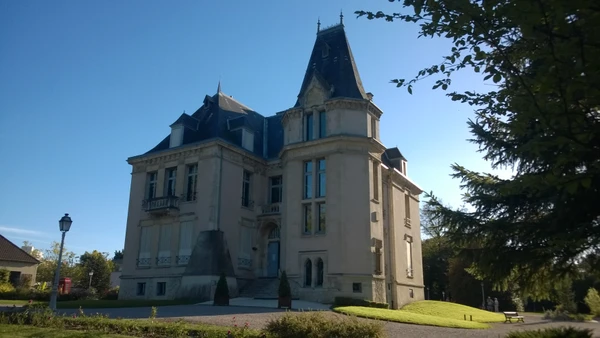 Vue extérieure professionnelle d'une façade de garage automobile moderne de petite à moyenne taille, situé en zone urbaine ou périurbaine. Le bâtiment affiche une devanture claire avec des portes de garage fonctionnelles, un parking avec quelques véhicules en attente de réparation. L'atmosphère doit être professionnelle et accueillante, reflétant un garage local établi et de confiance. La photo doit être prise de jour en conditions d'éclairage naturel.
